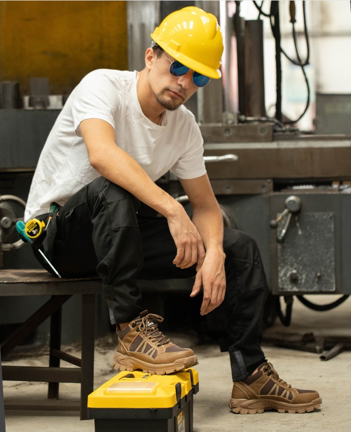 Industrie-Szene: Arbeiter mit gelbem Helm trägt Beige Boots, sitzt auf Kiste