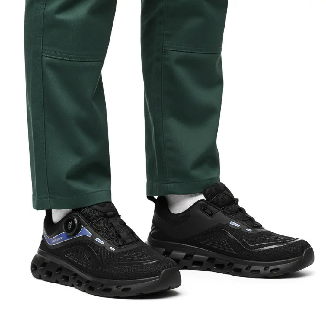 Schwarze Sicherheitsschuhe am Fuß eines Arbeiters mit grüner Hose